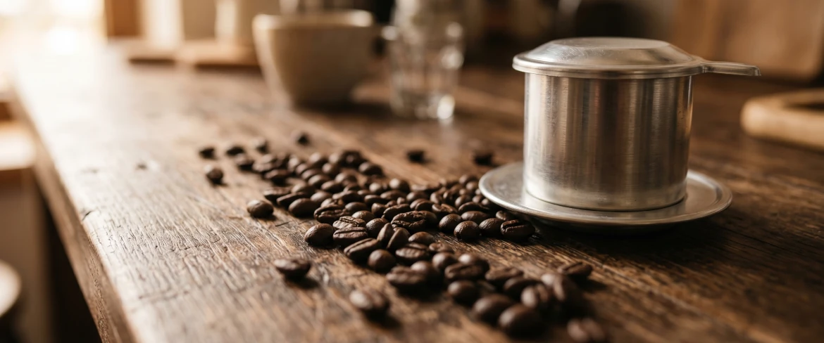 Rozsypane ziarna na drewnianym stole i zaparzacz phin do kawy po wietnamsku